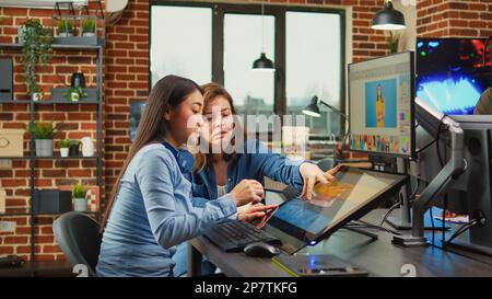 Female content creators editing professional images with retouching software and stylus pen, working on multimedia content. Diverse graphic artists processing photos using tablet and touchscreen. Stock Photo