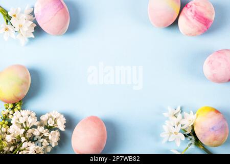 Colorful Easter eggs with spring blooming daffodils and white lilac on a blue background. Colored Egg Holiday border. Stock Photo