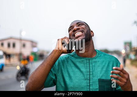 Excited young African man talking on smartphone outdoors, talks with family overseas. Stock Photo
