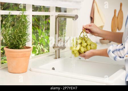 Woman washing grapes under tap water in kitchen sink, closeup Stock Photo