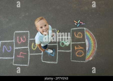 Little boy and colorful hopscotch drawn with chalk on asphalt outdoors, top view. Happy childhood Stock Photo