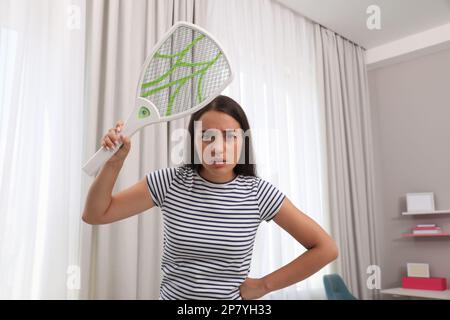 Young woman with electric fly swatter indoors. Insect killer Stock Photo