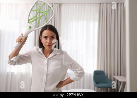 Young woman with electric fly swatter indoors. Insect killer Stock Photo