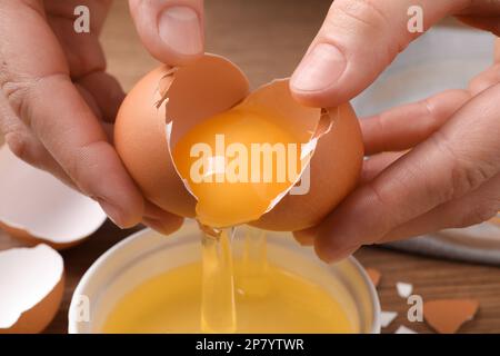 Woman separating egg yolk from white over bowl at table, closeup Stock Photo