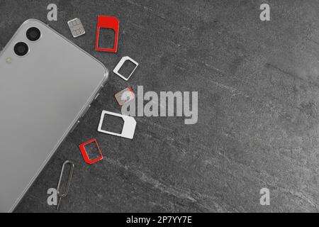 SIM cards, mobile phone and ejector tool on grey table, flat lay. Space for text Stock Photo