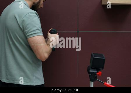 Man using cross line laser level for accurate measurement and drilling hole in brown wall, closeup Stock Photo