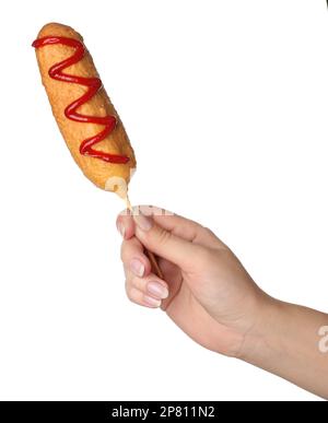 Woman holding delicious deep fried corn dog with ketchup on white background, closeup Stock Photo