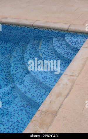 Semi-circular steps lead down into a refreshing hotel swimming pool, very welcome after enduring Mediterranean heat, June 2022. Stock Photo