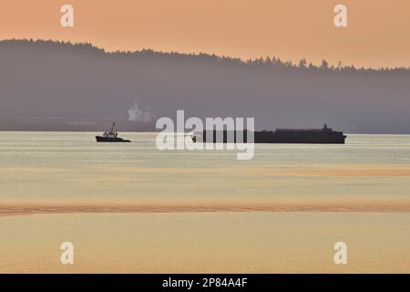 A tug boat pulling a barge in the warm toned morning light on the Stewart channel British Columbia Canada. Stock Photo