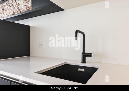 a black and white kitchen with brick wall in the back, sink is at the center of the room on the right hand side Stock Photo