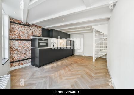 a kitchen and living room in an apartment with exposed brick walls, wood flooring and white painted ceilings Stock Photo