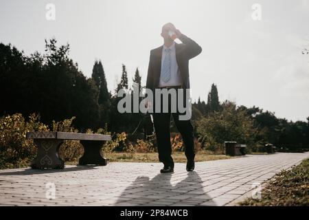 Mature entrepreneur drink coffee in autumn park. Senior executive rest in city park. Stock Photo