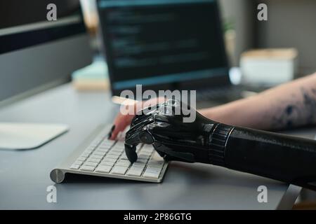 Close-up of girl with prosthetic arm typing on keyboard, she using computer to do online work Stock Photo