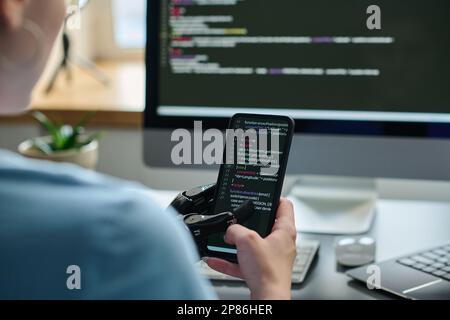 Close-up of IT specialist working with codes on smartphone connecting it with computer and developing software Stock Photo