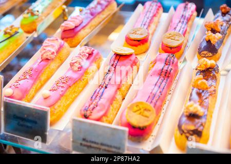 eclairs with colorful topping a lot on shop window, store shelf. french dessert, different types, close-up Stock Photo