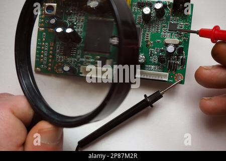 Technician working on microchip board with magnifying glass. Repair of a computer. Trouble finding and test with a multimeter on an electronic card. Stock Photo