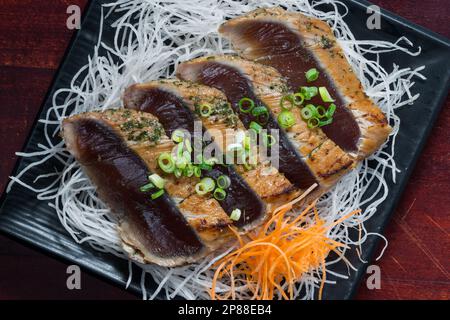 Japanese style of temaki with fillet of mackerel fish served julienned vegetables and leek on black plate, Asian food, traditional Japanese food, top Stock Photo