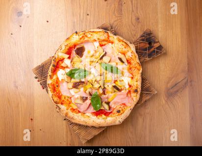 Capricciosa pizza with cheese, bacon, tomatoes, mushrooms and basil, italian meal. Baked neapolitan pizza with artichokes served on wooden board. Top Stock Photo