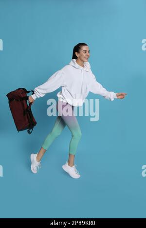 Beautiful woman with sports bag running on light blue background Stock Photo