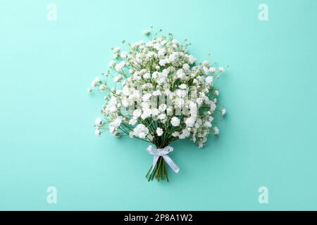 Beautiful gypsophila flowers tied with ribbon on turquoise background, top view Stock Photo