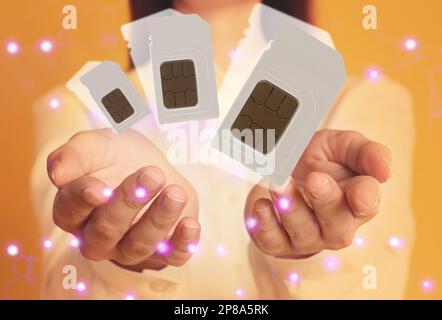 Woman demonstrating SIM cards of different sizes on yellow background, closeup Stock Photo