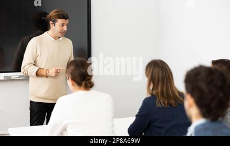 Competent male tutor teaching students in college classroom Stock Photo