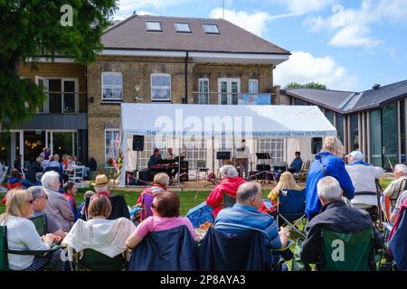 People watch Fats Rollini Jazz & Blues Band perform under a marquee in Pinner Park for Jazz in the Park concert,  sponsored by Pinner Association. Stock Photo