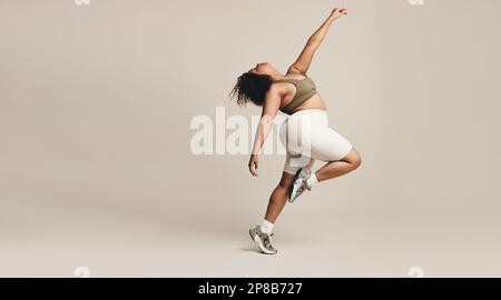 Young woman dancing in a studio, wearing fitness clothing. Young female expressing her self-assurance and body confidence, effortlessly finding her fl Stock Photo