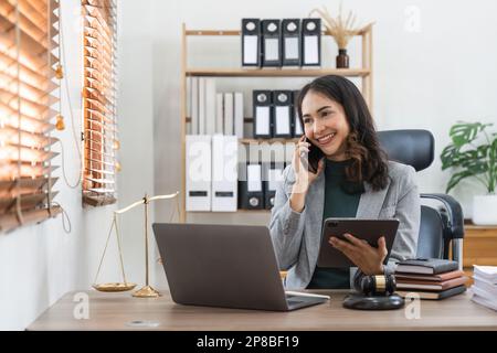 Female lawyer works in office or court, checks clients contracts, Calling by phone. Asian successful business lady, statuette of Themis, goddess of Stock Photo