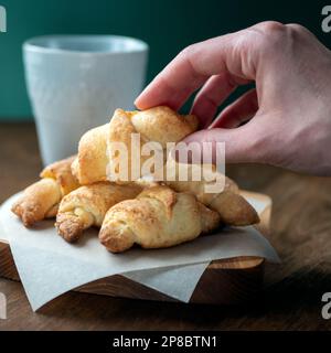 Miniature crescent-rolled pastry in hand, selective focus. Mini croissants or rugelaches. Stack of delicious golden-brown cookies Stock Photo