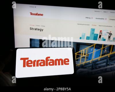 Person holding cellphone with logo of Finnish battery chemicals company Terrafame Oy on screen in front of webpage. Focus on phone display. Stock Photo