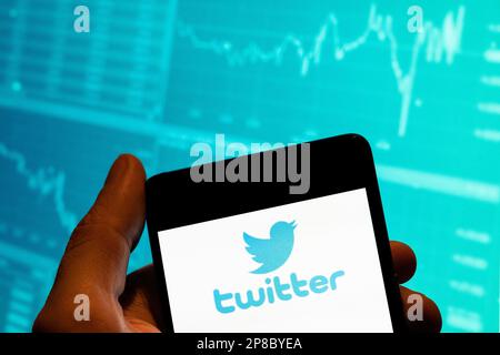 In this photo illustration, the American online news and social networking service Twitter logo is seen displayed on a smartphone with an economic stock exchange index graph in the background. Stock Photo