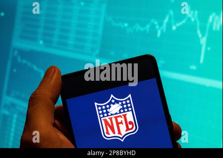 In this photo illustration, the American football league, The National Football League (NFL) logo is seen displayed on a smartphone with an economic stock exchange index graph in the background. Stock Photo