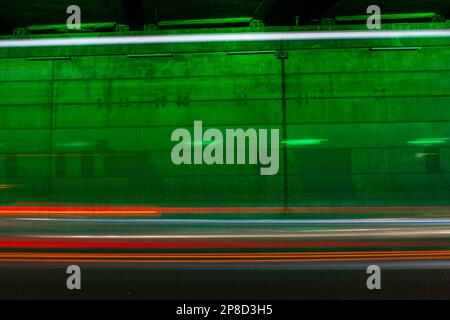 Car light trails in front of a wall illuminated by green light with space for text. Suitable as a background image. Stock Photo
