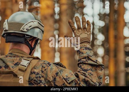 Modern warfare soldier officer is showing tactical hand signals to silently give orders and alers for squad team forest enviroment Stock Photo