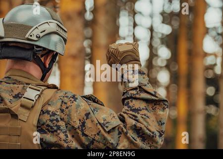 Modern warfare soldier officer is showing tactical hand signals to silently give orders and alers for squad team forest enviroment Stock Photo
