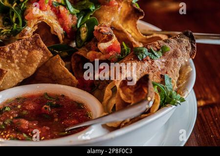 Close-up of a plate of crisps with meat, melted cheese, herbs, green chilli and tomato salsa dip Stock Photo