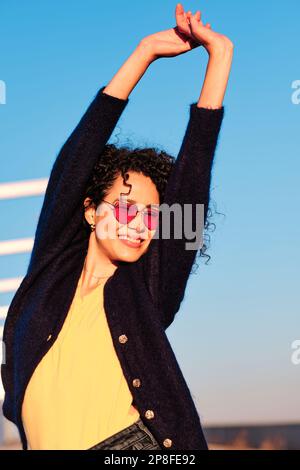Happy woman raising arms standing outdoors on a sunny day Stock Photo