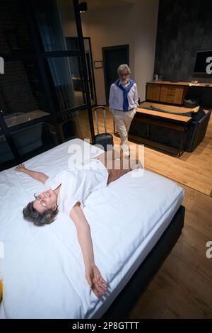 Happy elderly lady in a hotel room lies on bed Stock Photo
