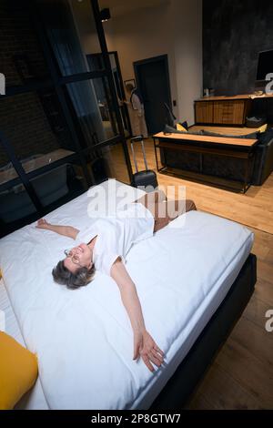 Happy traveling lady resting on bed with arms outstretched Stock Photo
