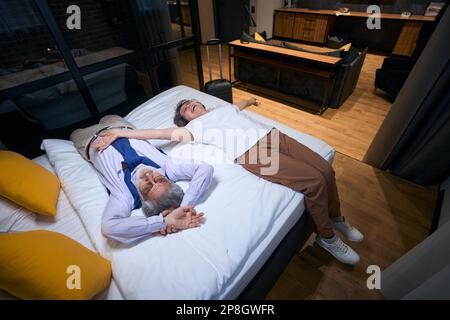 Tired from road, but happy elderly spouses are resting on bed Stock Photo