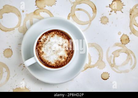 A cup of tasty cappuccino coffee stands on a white background with coffee stains and splashes. Flat lay layout with copy space Stock Photo