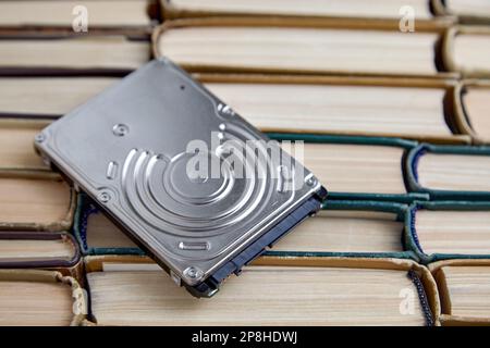 The hard drive of the computer lies on a pile of shabby paper books. Carriers of information from different eras. Stock Photo