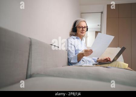 Cute grandmother is studying distance learning at home on couch Stock Photo