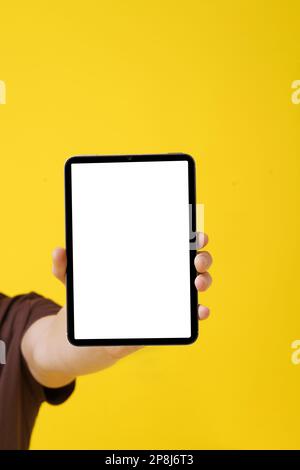 close-up image of a man's hand holding a blank screen Tablet PC against a yellow background, showcasing technology concept and digital revolution. Copy Space concept for advertising. . High quality photo Stock Photo
