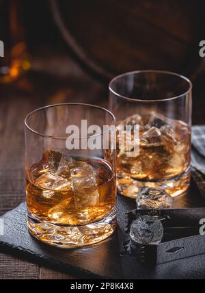 Two glasses of whiskey with ice on a black slate board with wooden background Stock Photo