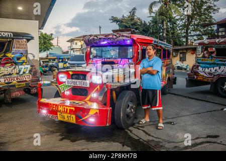 Mark stands next to his traditional jeepney and poses for the camera in Metro Manila. For decades, commuters have relied on jeepneys, a vibrant and iconic method of transportation in the Philippines. It is regarded as an iconic representation of Philippine transportation and has evolved into a national symbol. The first Jeepneys were converted American military jeeps that had been abandoned in the Philippines following World War II into unique public transit vehicles that could accommodate up to 20 passengers. On its decade run, the government is pushing a modernization initiative to replace Stock Photo