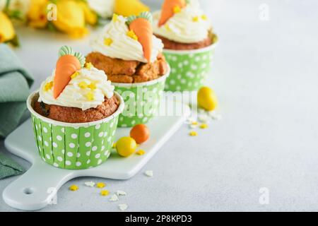 Carrot cake cupcakes for Easter. Carrot cupcakes with cream cheese frosting decorated with tiny marzipan carrots on white background. Happy Easter and Stock Photo
