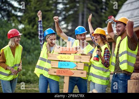 A group of cheerful both female and male builders posing for a photo at a cottage construction site on a beautiful day. Construction, building, worker Stock Photo