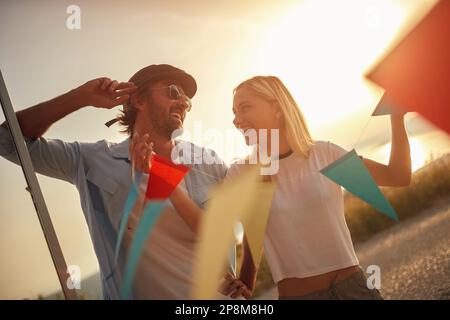 young adult caicasian couple having fun at sunset, playing with little flags Stock Photo